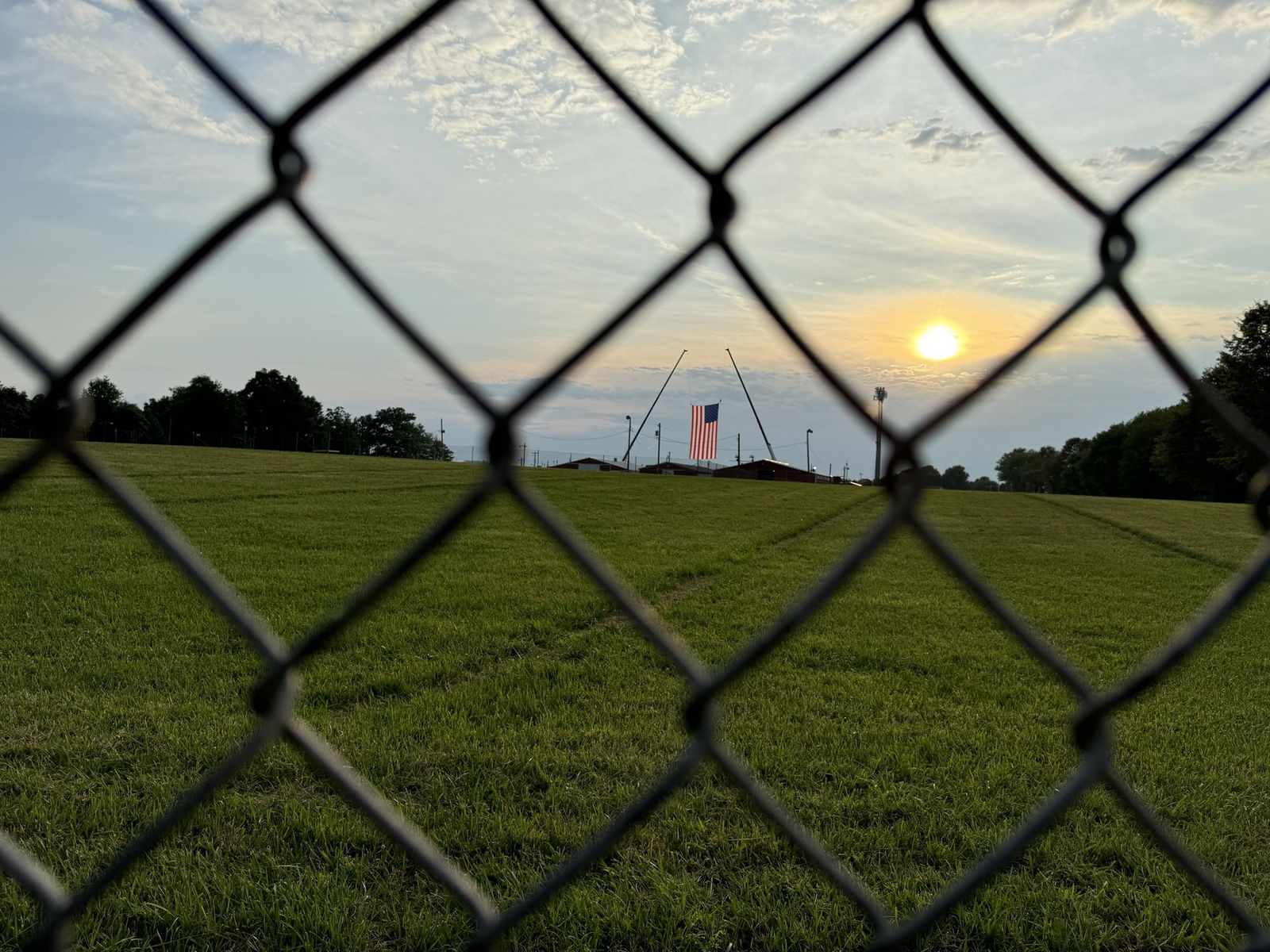 A large American flag hangs over a stage in the distance behind a wire fence