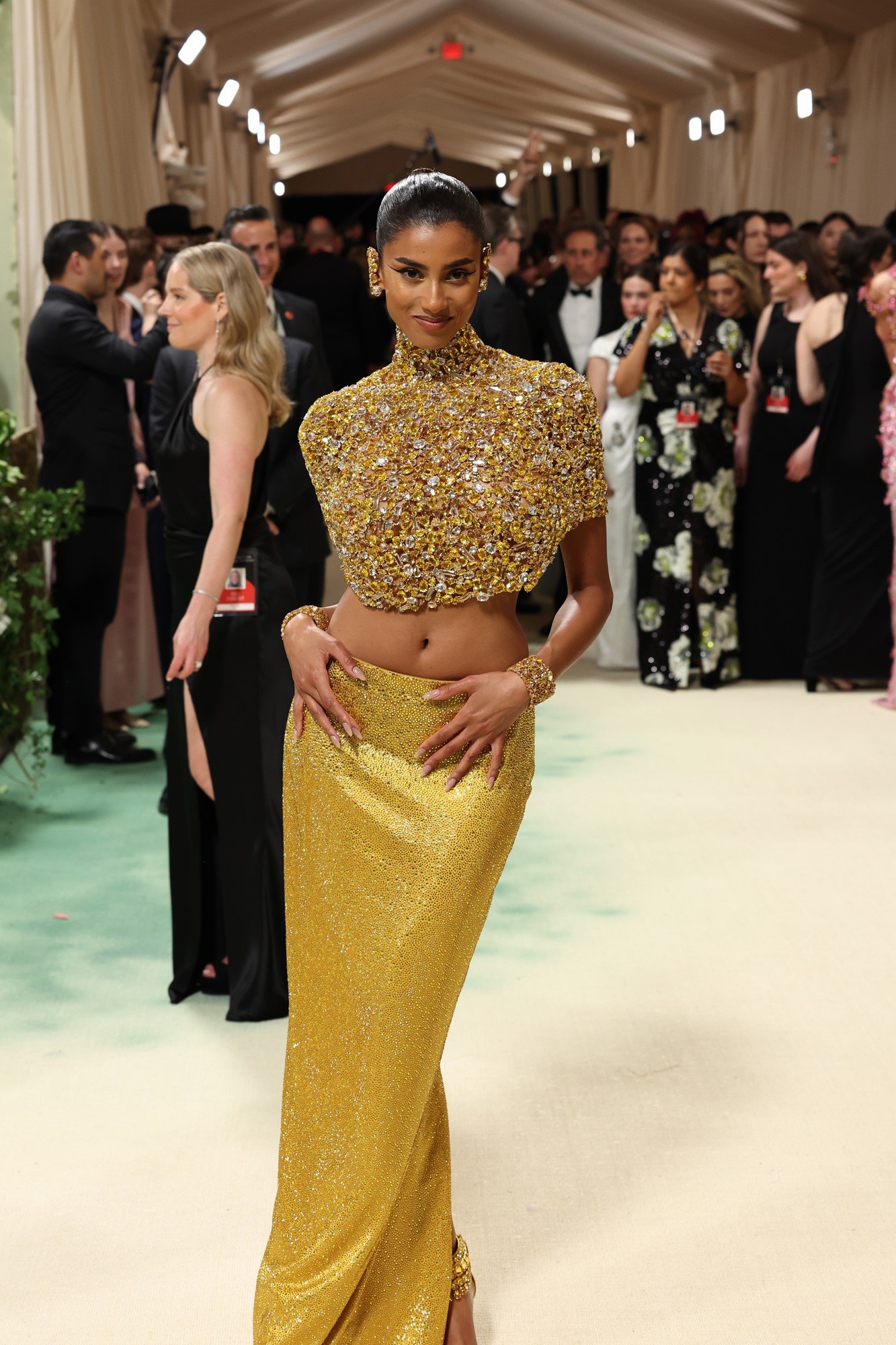 Imaan wears a gold bedazzled top and a low slung gold skirt.