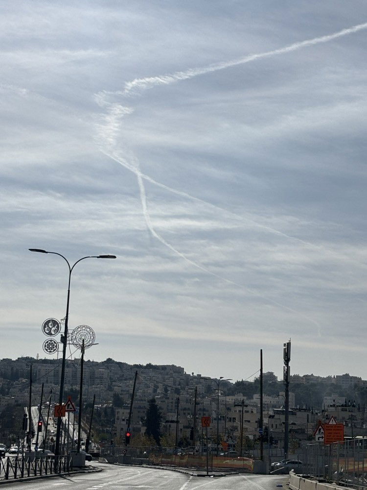 A con trail from a fighter jet creating a ribbon over the skies of Jerusalem.