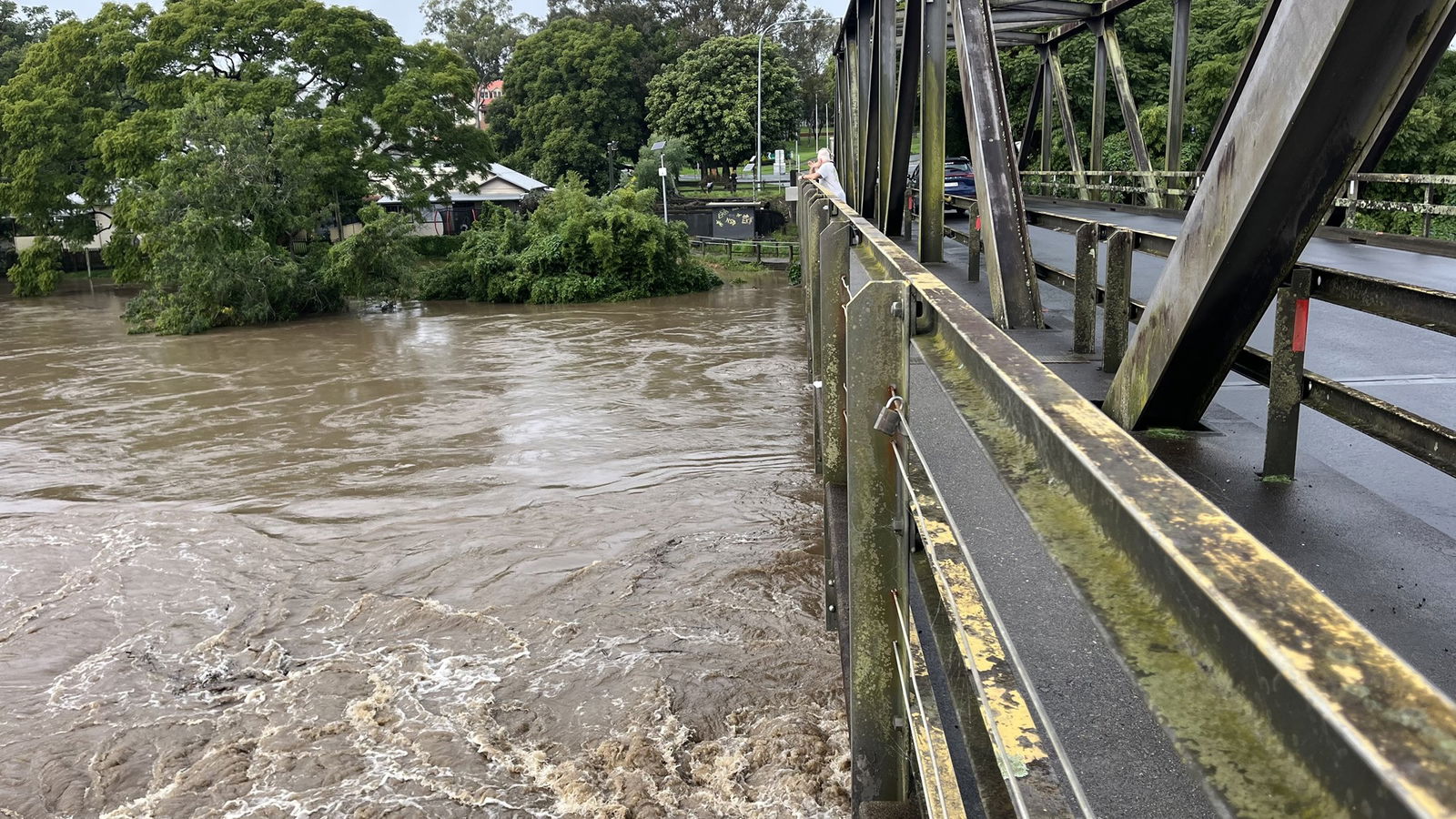 Waters churn in a brown river near a bridge