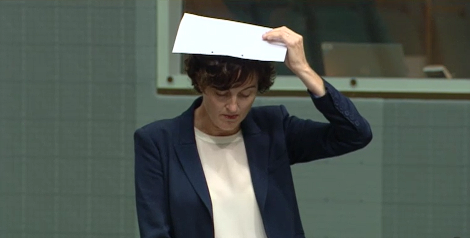 A middle-aged woman in a suit holds a piece of paper over her head.