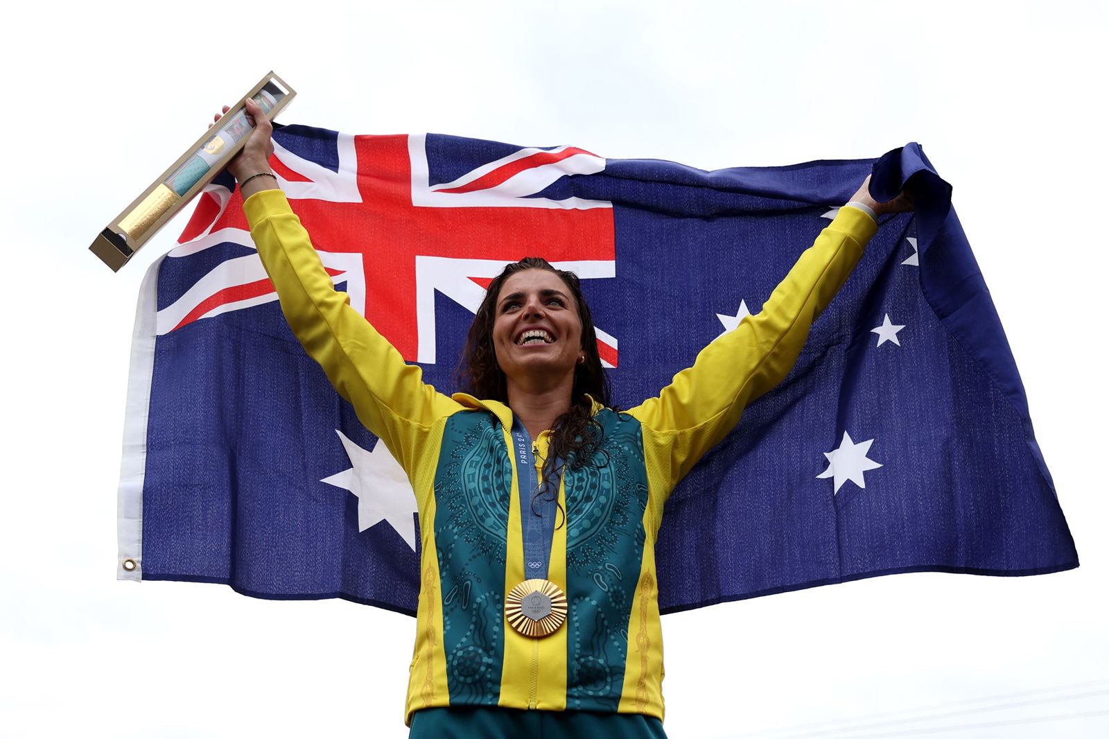 Jess Fox smiles while holding up the Australian flag behind her as she wears a gold medal after the C1 canoe slalom final.
