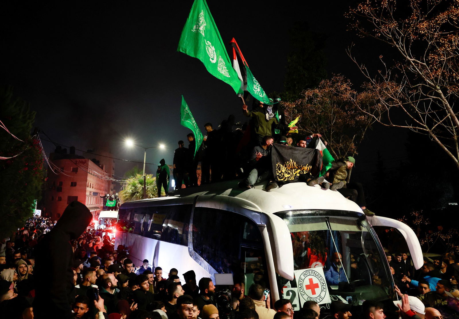 A mass of people, some waving green flags, mass around and on top of a white van at night.