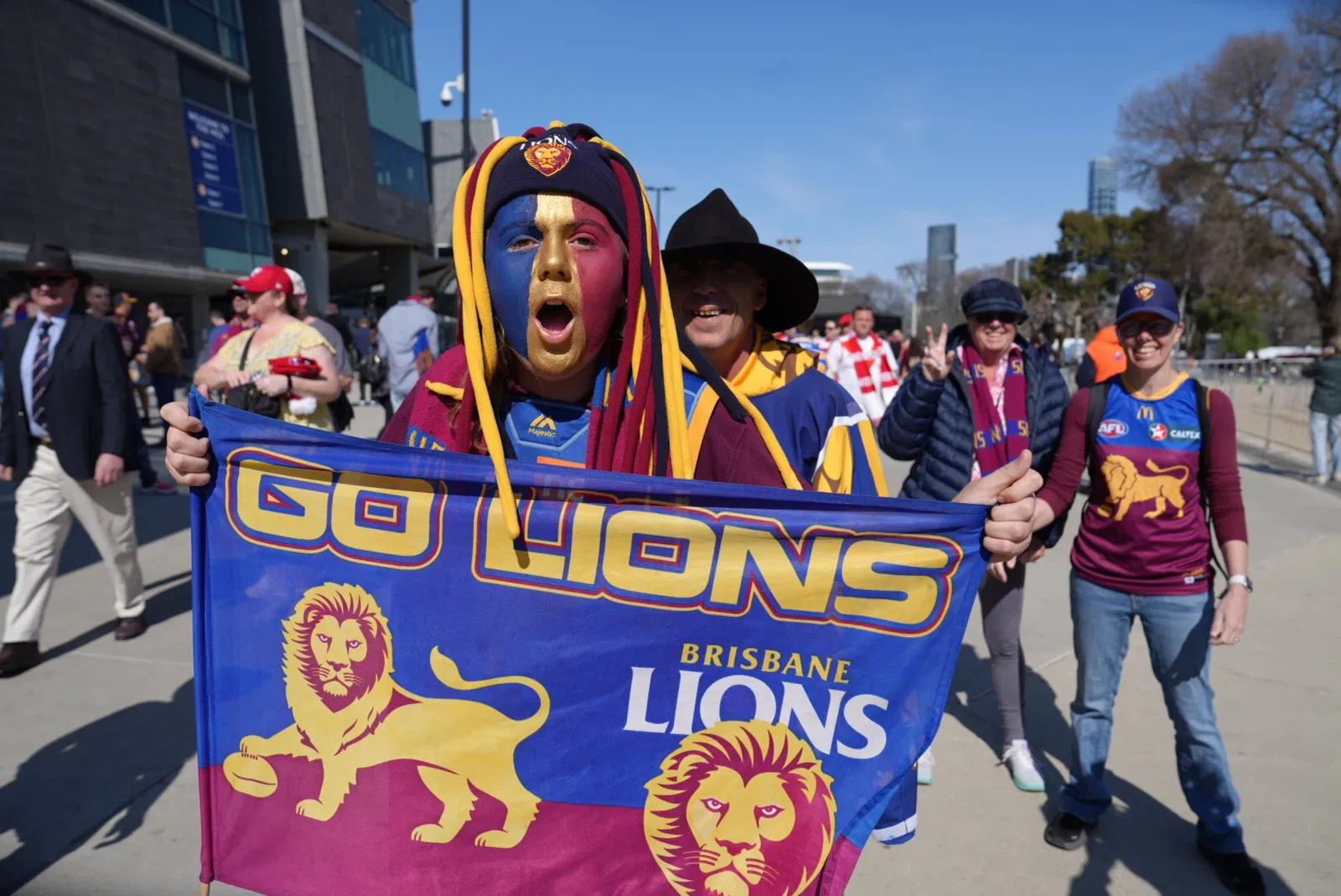 Wayne Ford waves a Brisbane Lions flag, his face painted in their colours of burgundy, blue and gold.