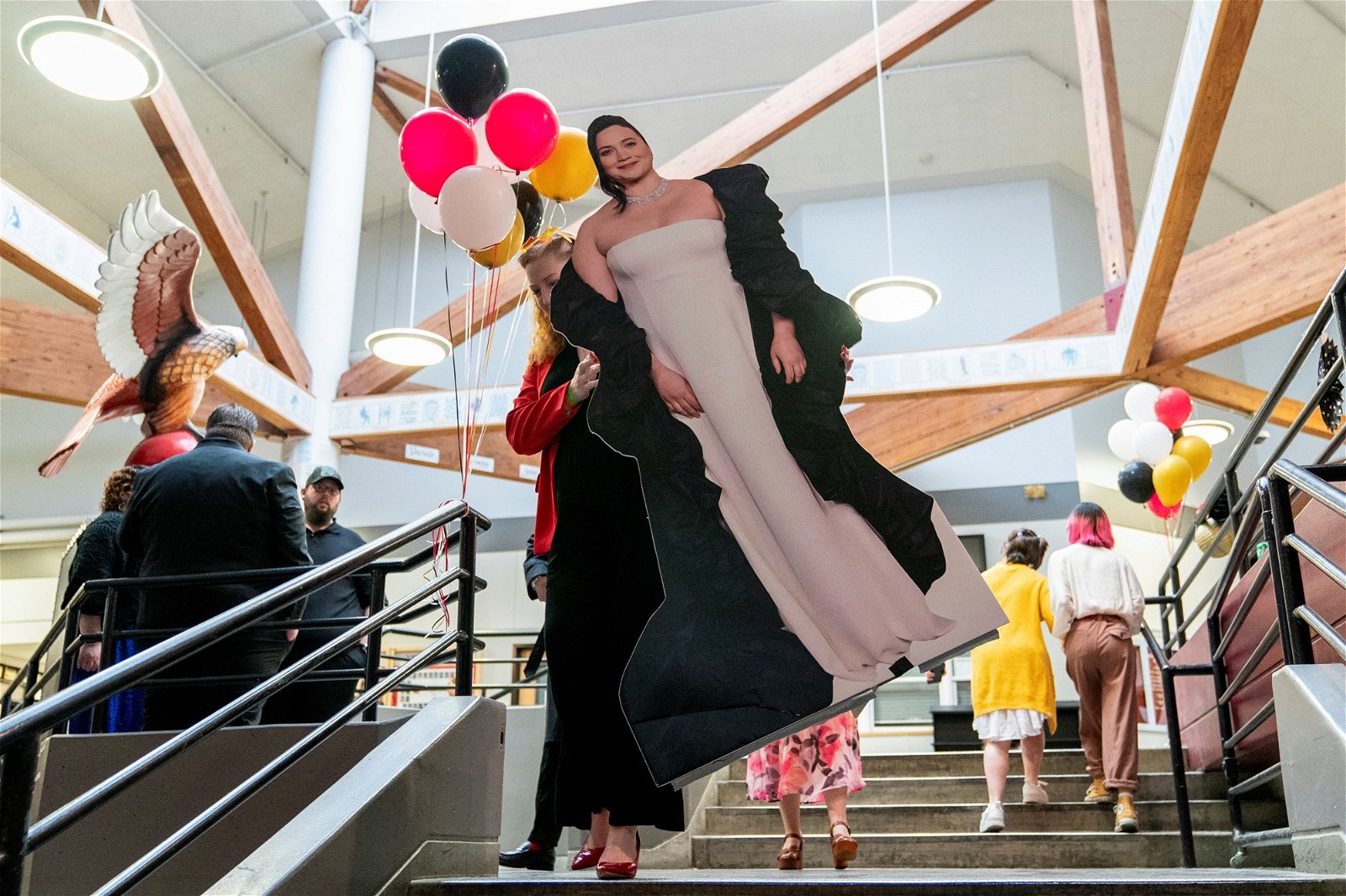 A woman walks a lily gladstone cardboard cut out down a stairs at a school