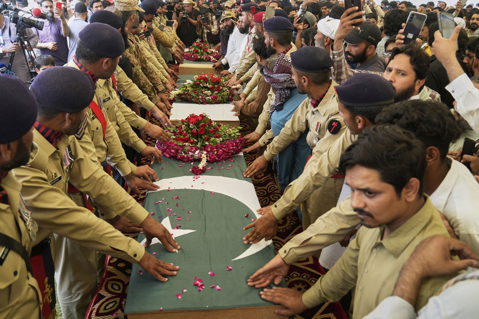 Men dressed in army fatigue hold their hands on three coffins which are drapped in Pakistani flags and covered with flowers