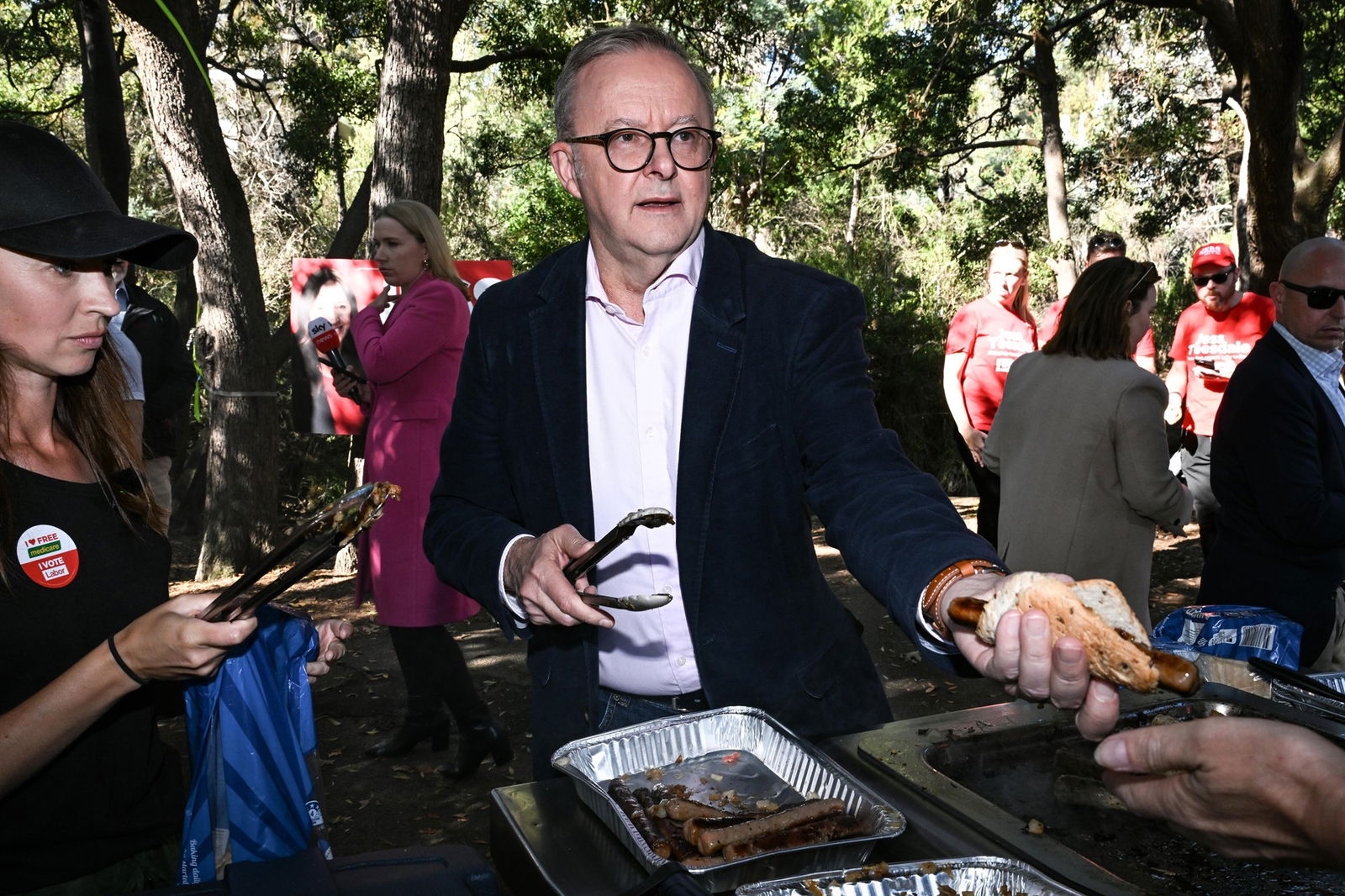 Anthony Albanese holds a pair of tongs as he hands out a sausage in bread.