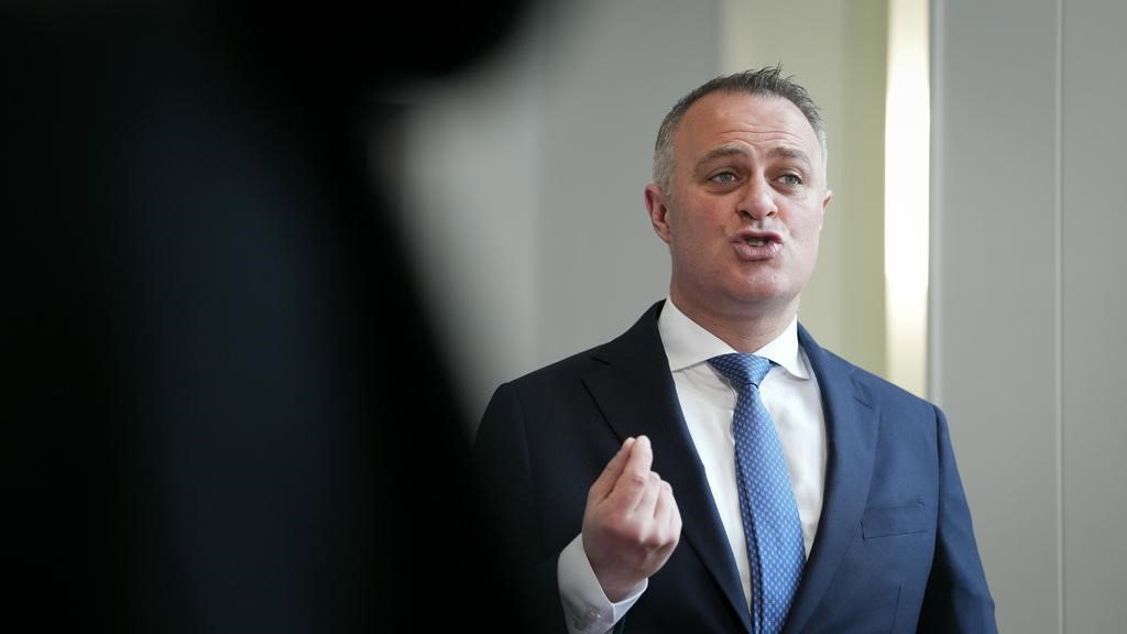 Man in hallway making a gesture with his hand as he speaks.