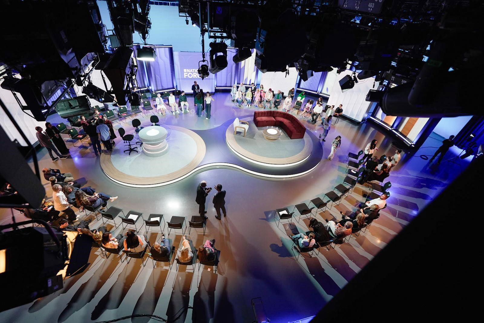 An overhead shot of the studio, with the audience seated in a circle around two sets.