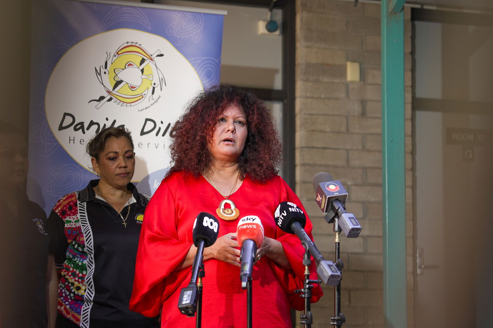 A woman in a red dress stands behind microphones