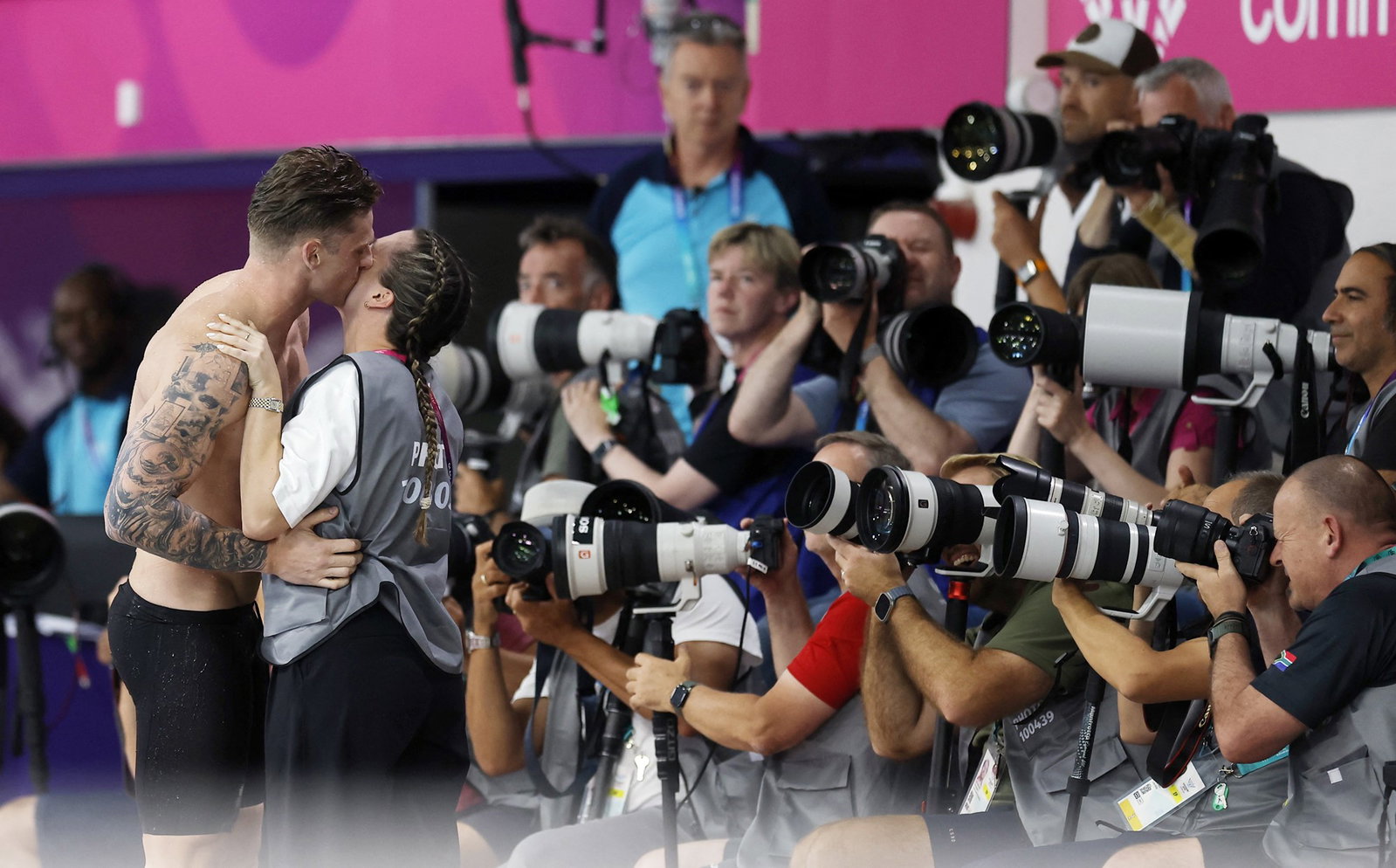 Sam Williamson hugging and kissing his partner with photographers taking pics