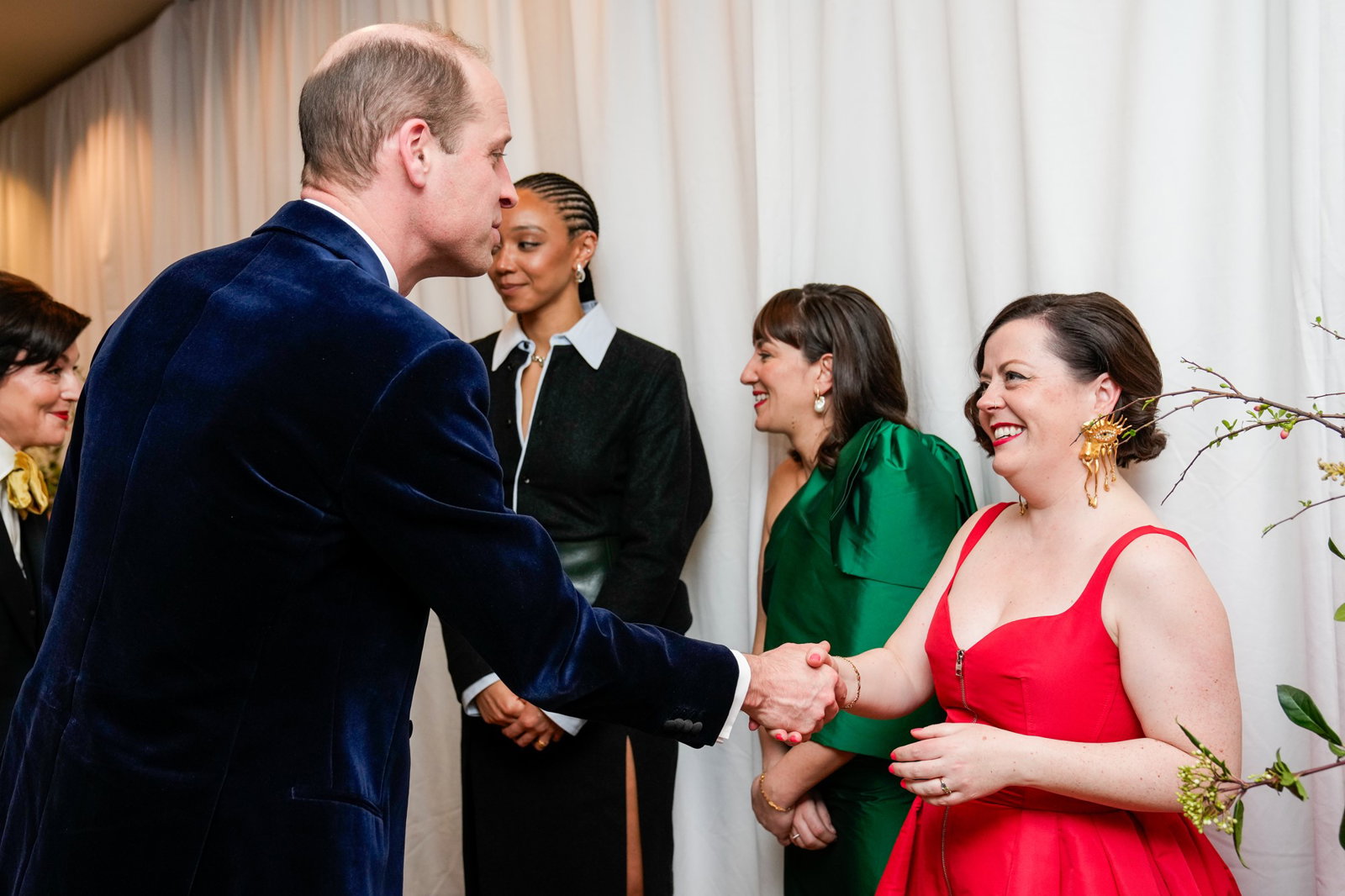A woman in a red dress shakes hands with prince william