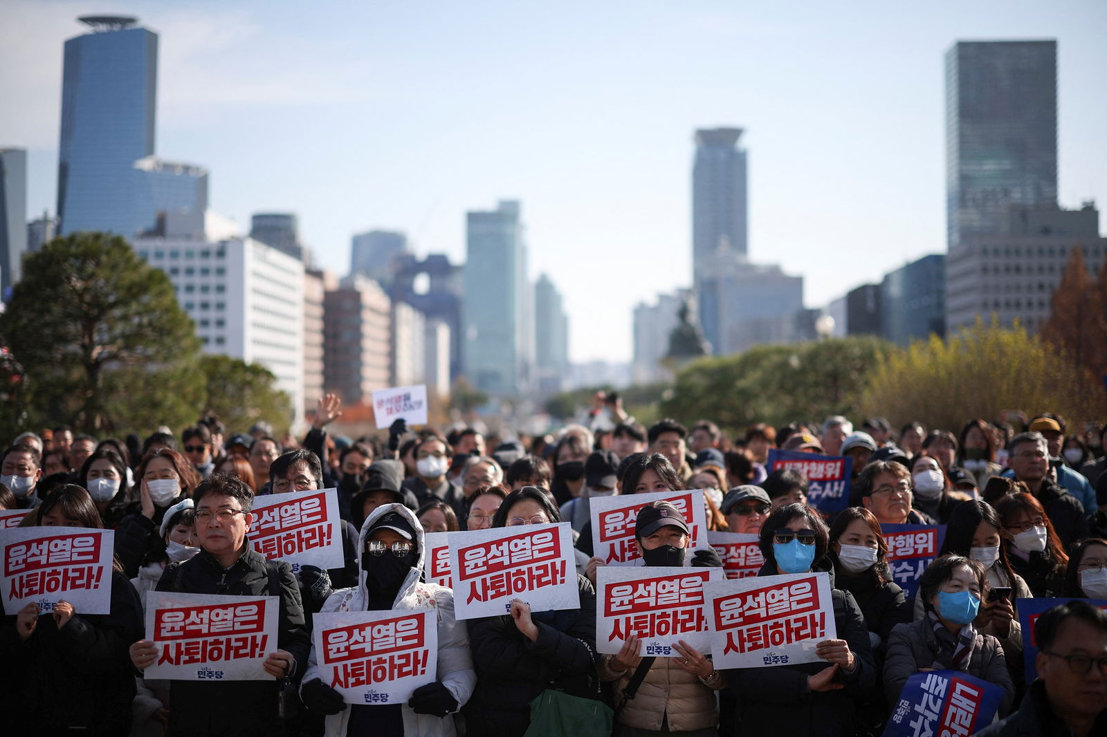 a crowd of people pictured from the front holding red and white signs with Korean script