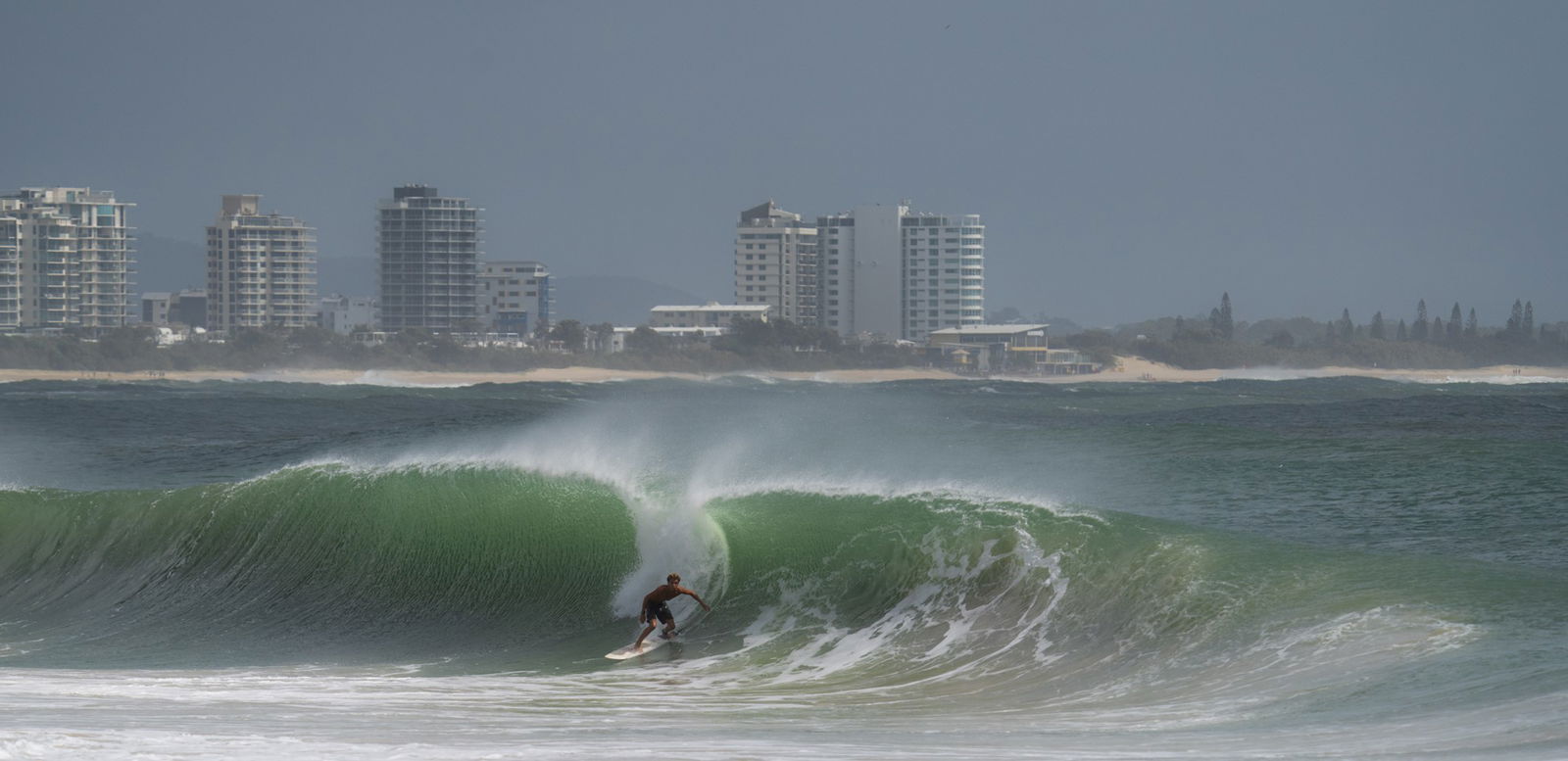 A man suring a wave. Apartments in the background. 