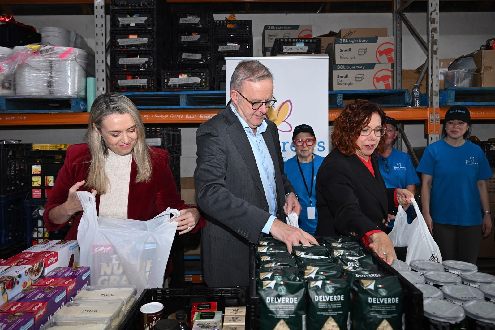 Anthony Albanese, Jodie Haydon and Amanda Rishworth fill plastic bags with food in a warehouse.