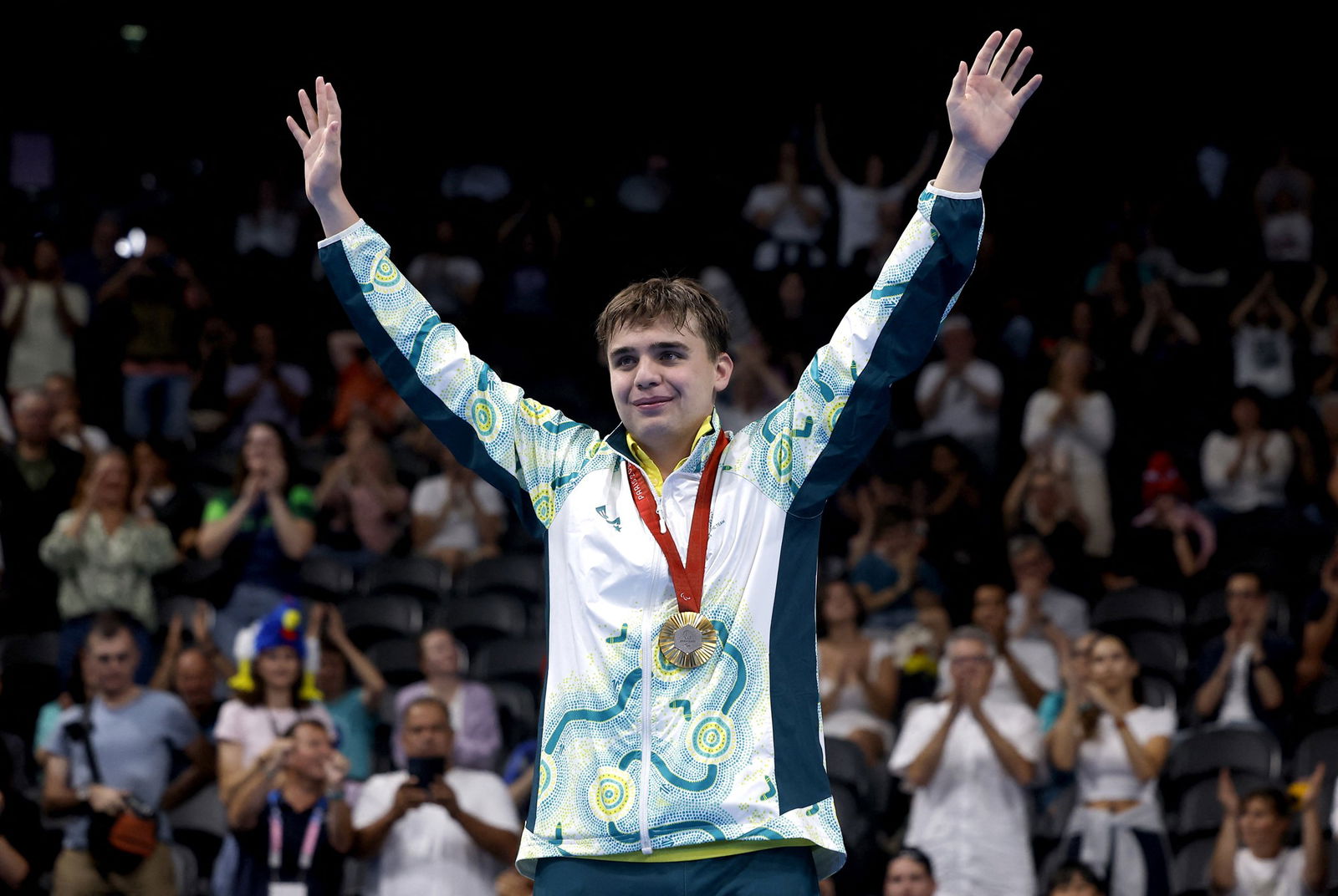 Callum Simpson with a gold medal around his neck, raises his arms in celebration