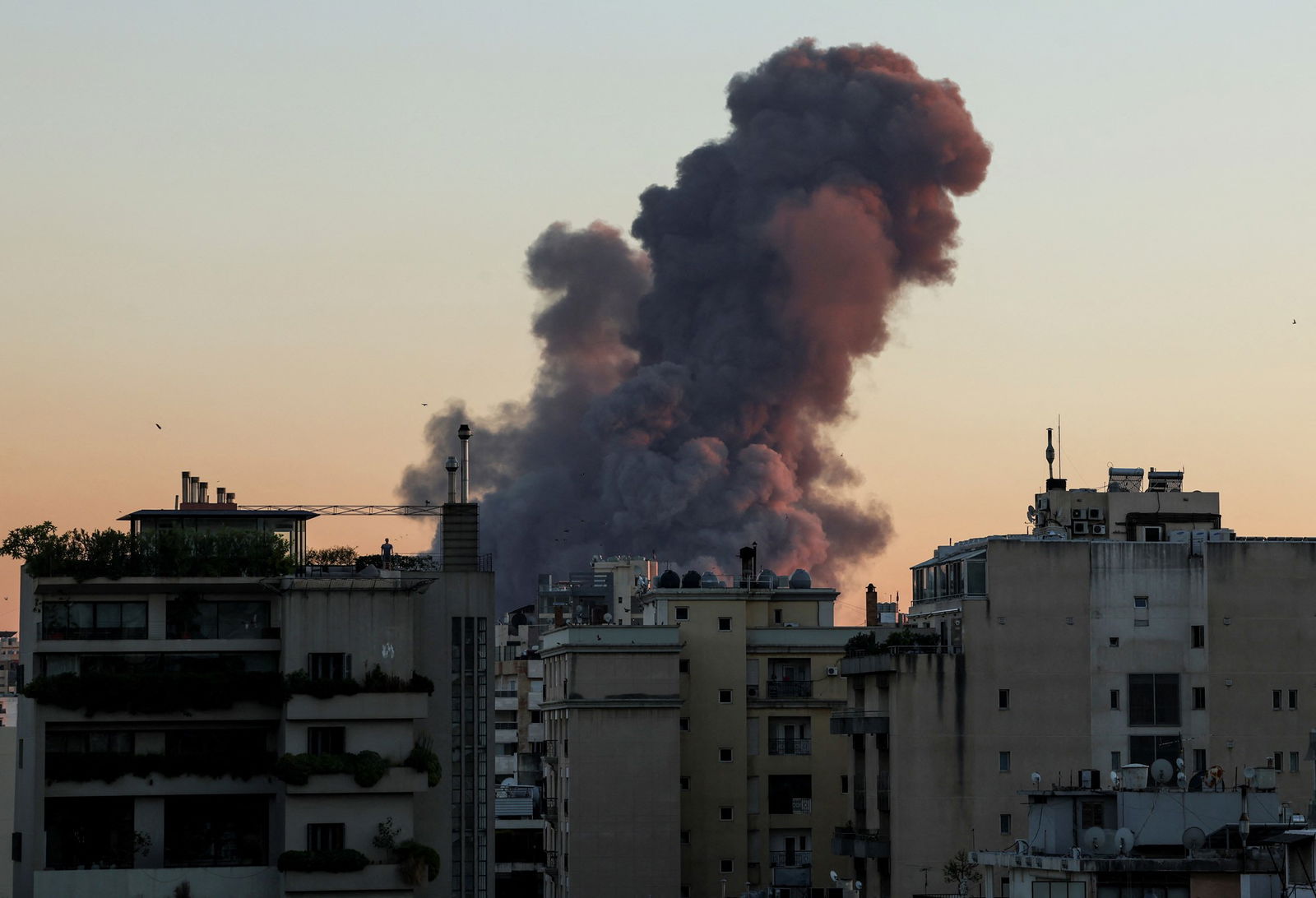 A large plume of smoke rises over several houses.