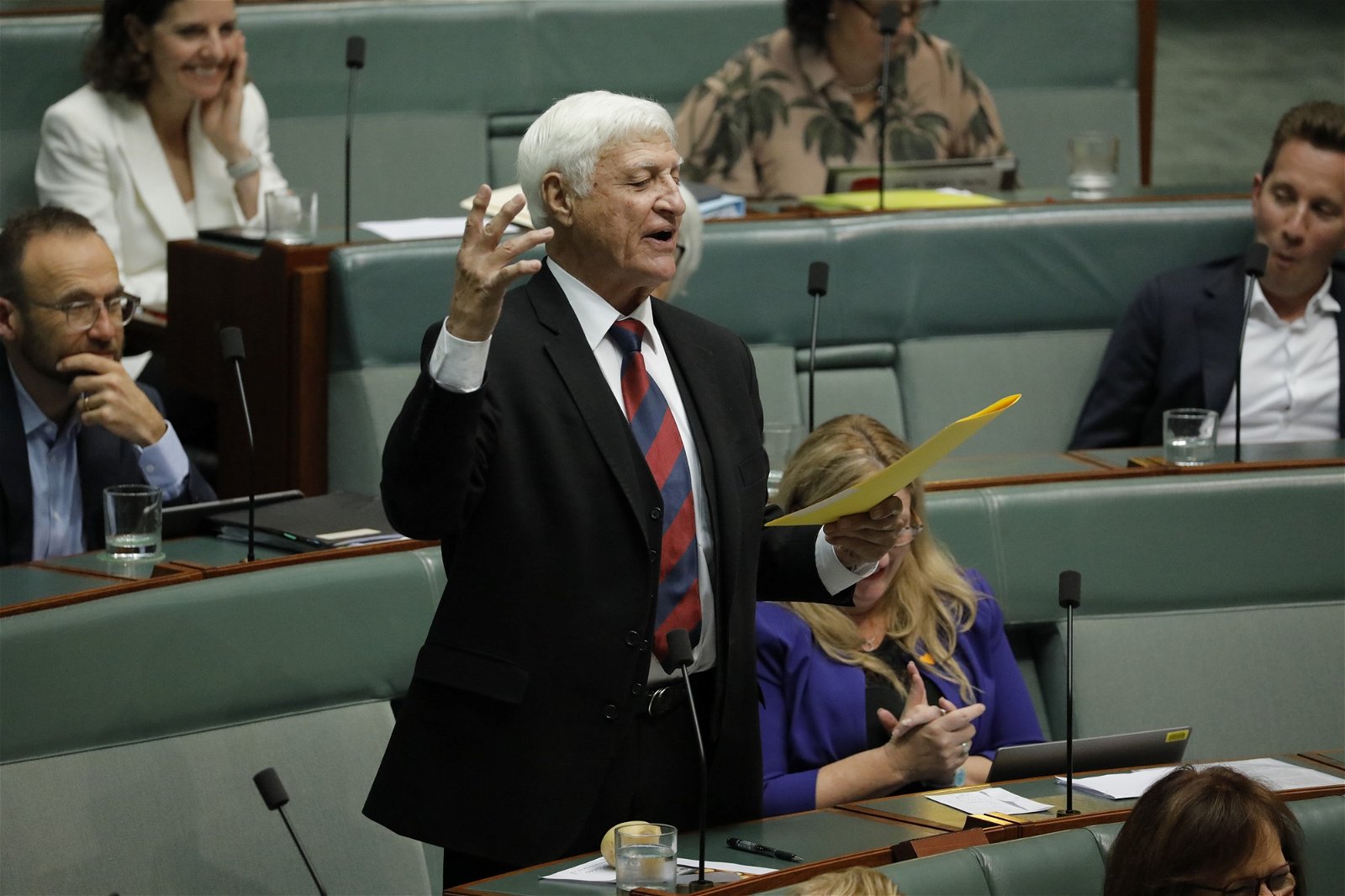 An older man in a suit delivers a speech with flare in parliament.
