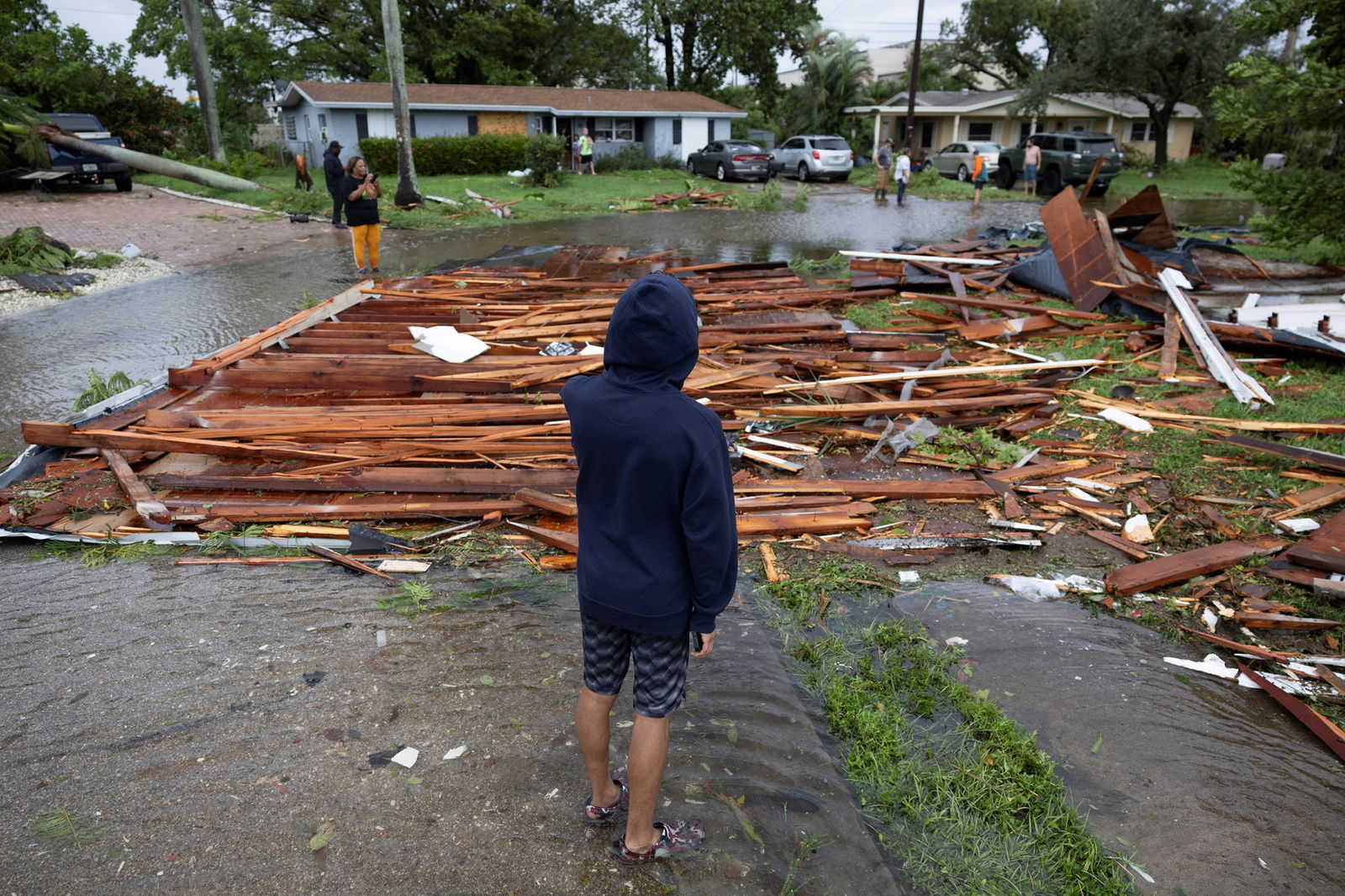 A man looks at a roof on a street from a nearby house, debris covers road