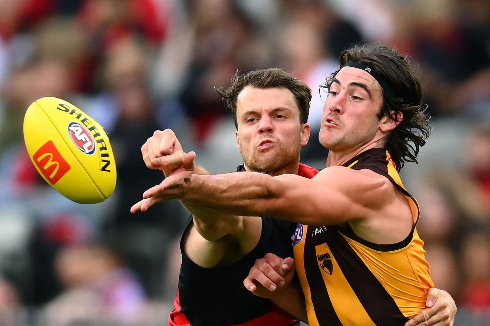 An Essendon player contests the ball with a Hawthorn opponent.