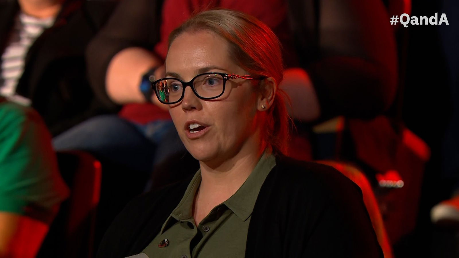 A woman in black glasses and a green shirt speaks