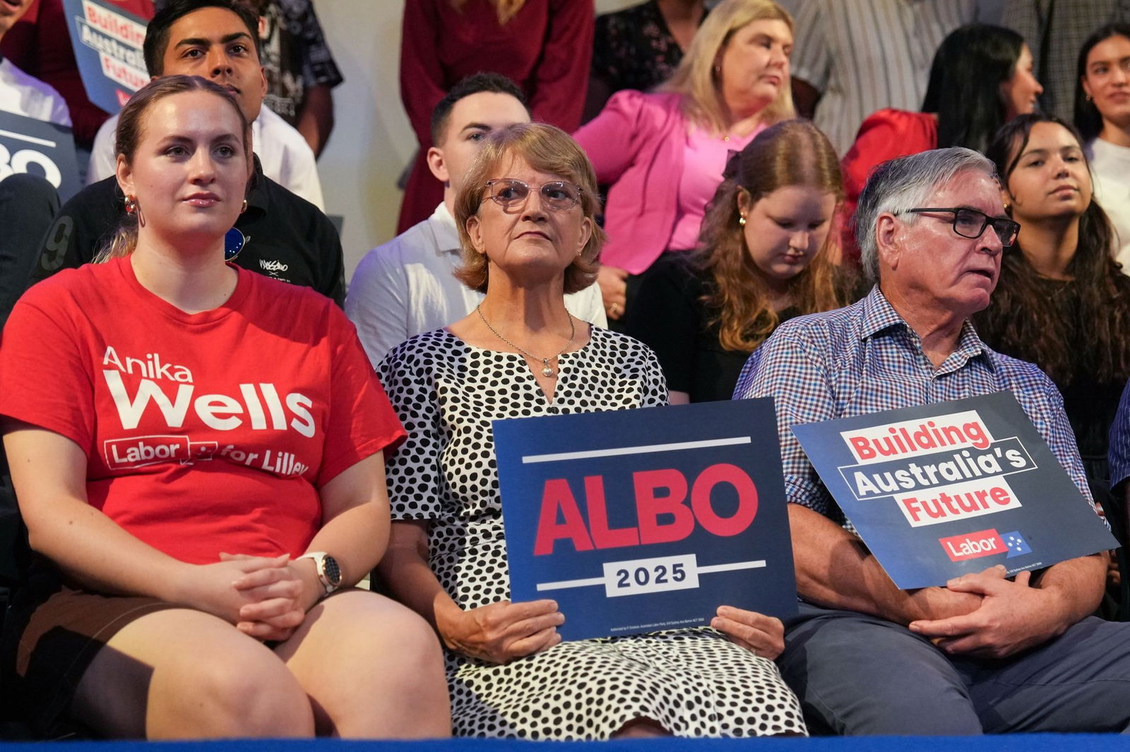 A row of Labor supporters sit in the audience, resting political signs in their laps