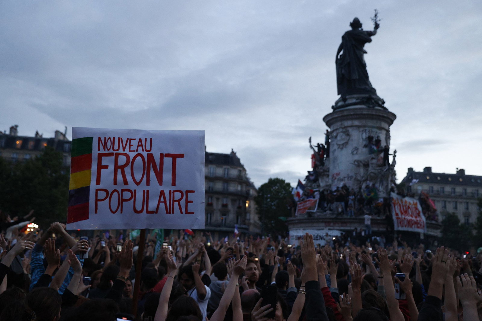 A crowd holds up a sign saying 'nouveau front populaire'