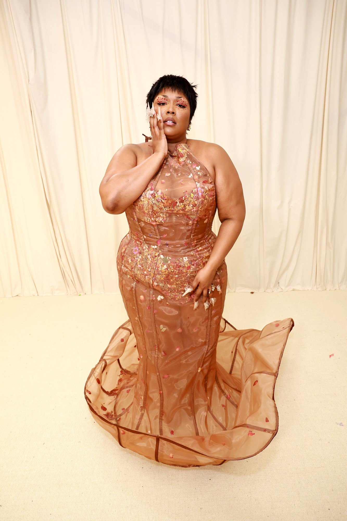 Lizzo poses with her hand on her cheek in her sequined gown.