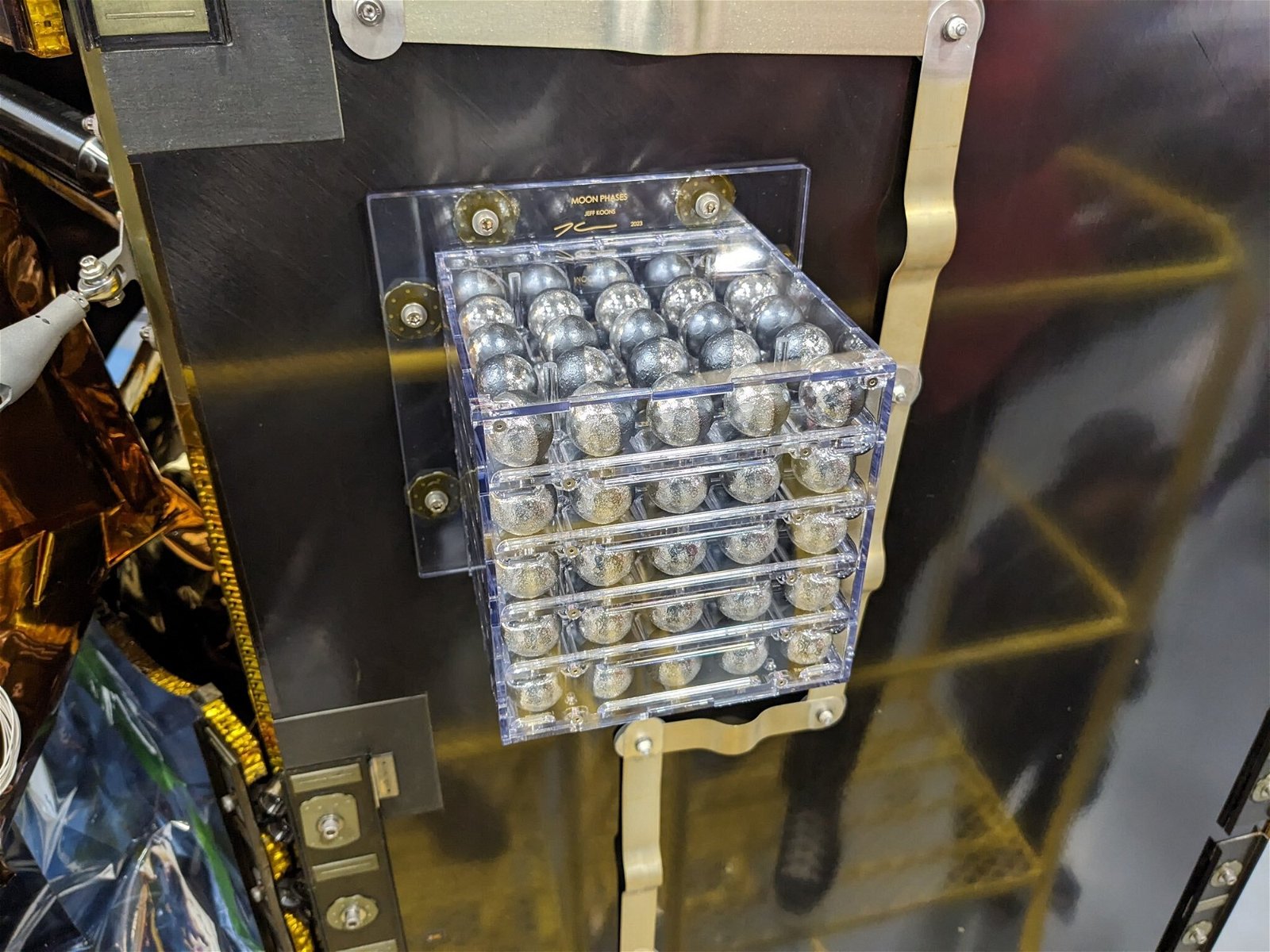 A group of small spheres in a clear box on the side of a spacecraft