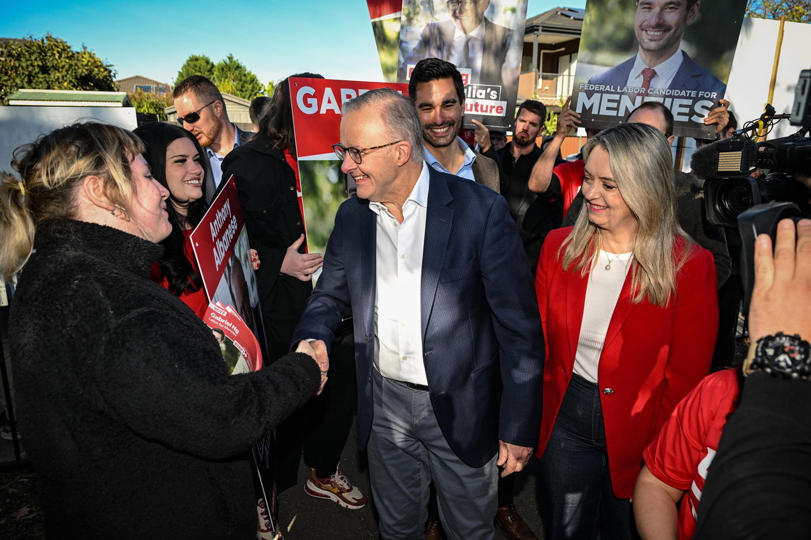 Anthony Albanese and Jodie Haydon smiling while greeting supporters, surrounded by Labor campaign placards