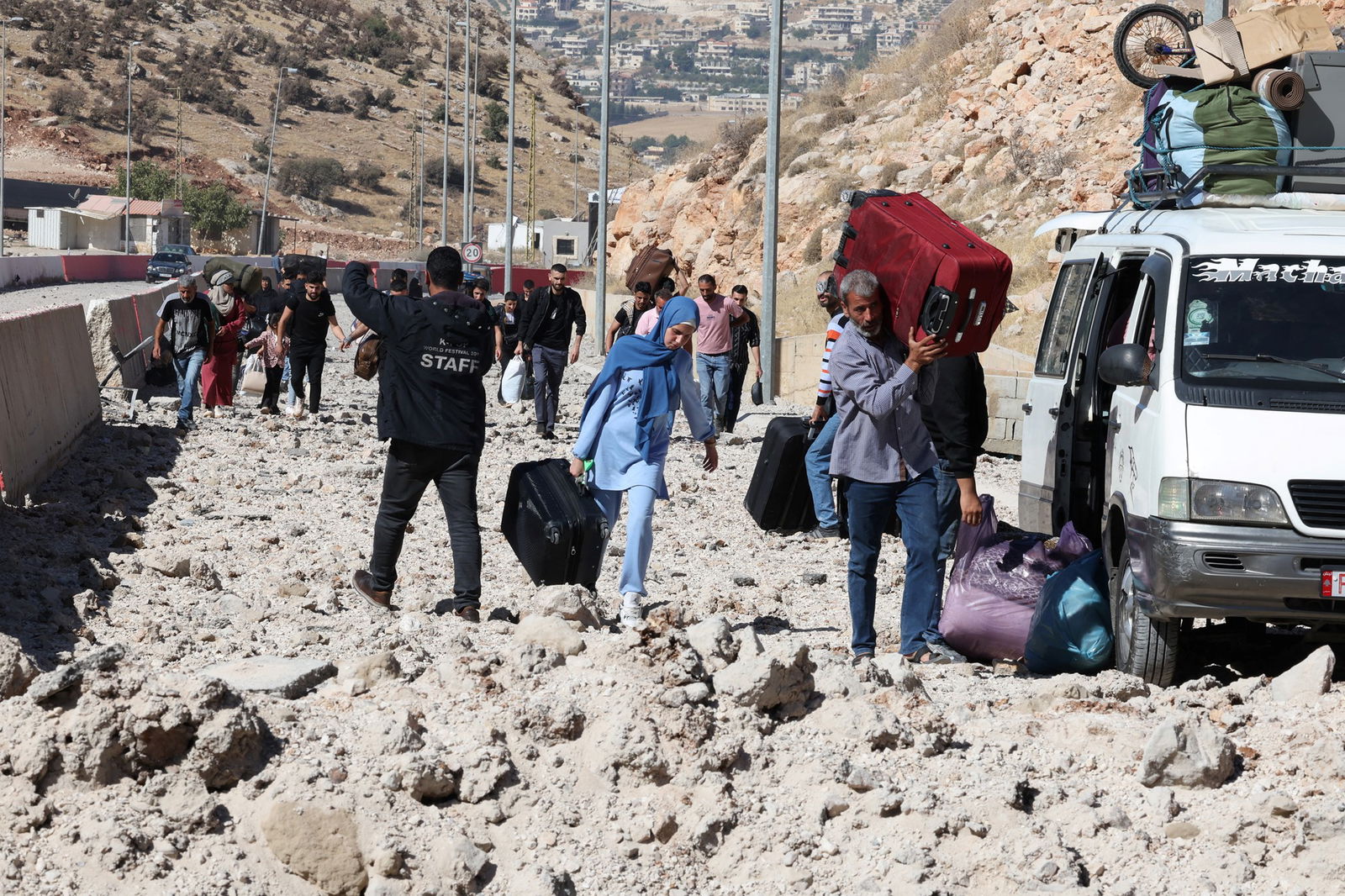 A small crowd carrying backs walking on rubble.