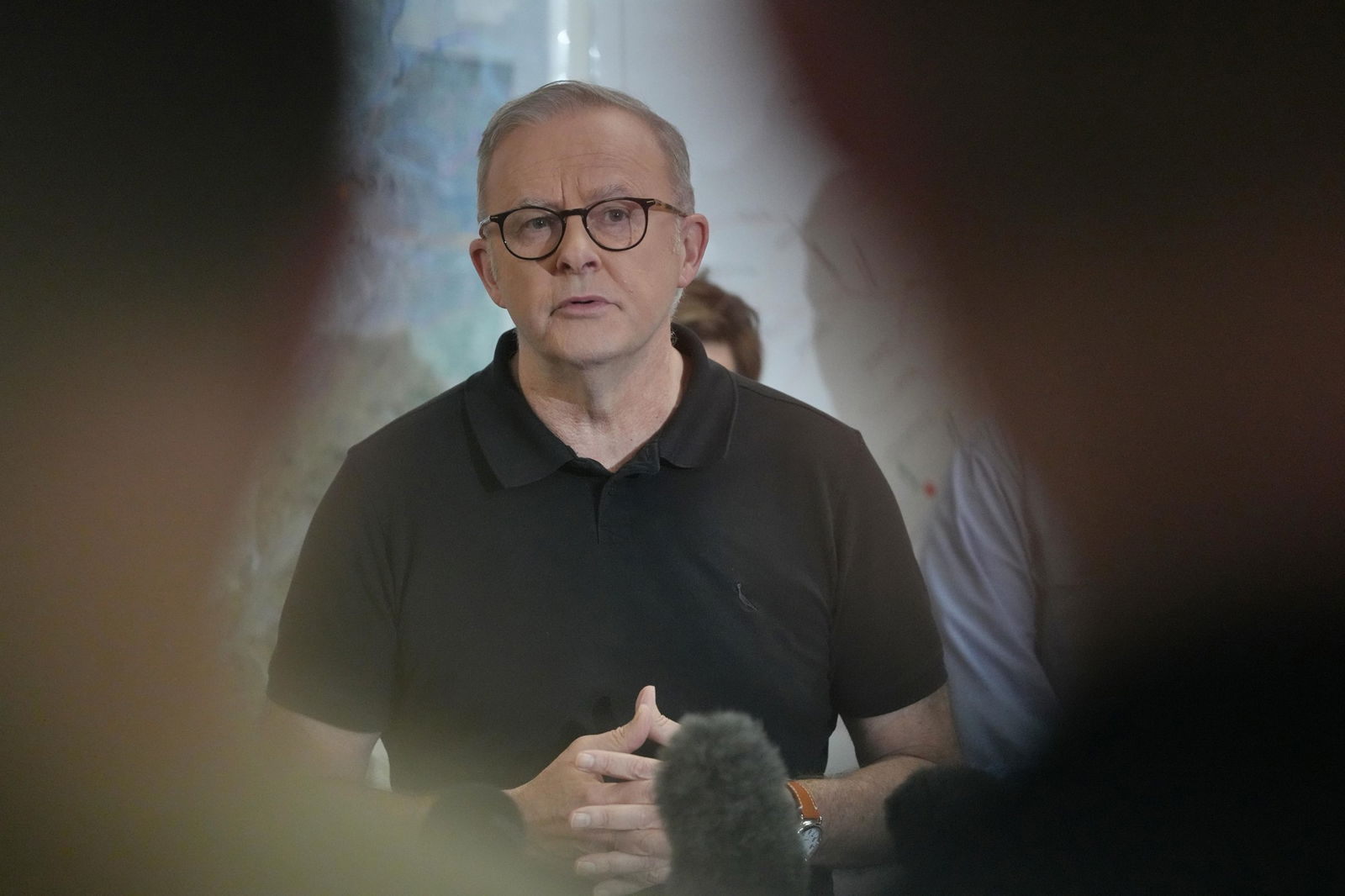 The prime minister speaks to the media while wearing a black polo shirt.