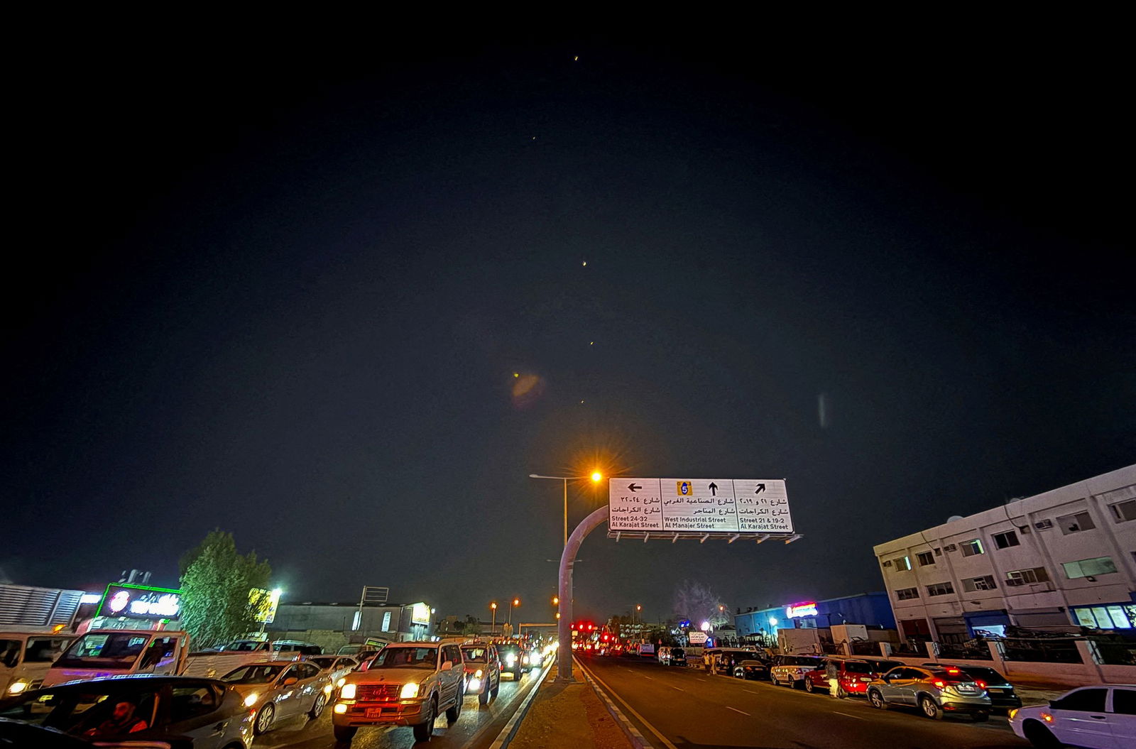 Small bright yellow dots are seen streaking through the night sky above a busy multi-lane highway