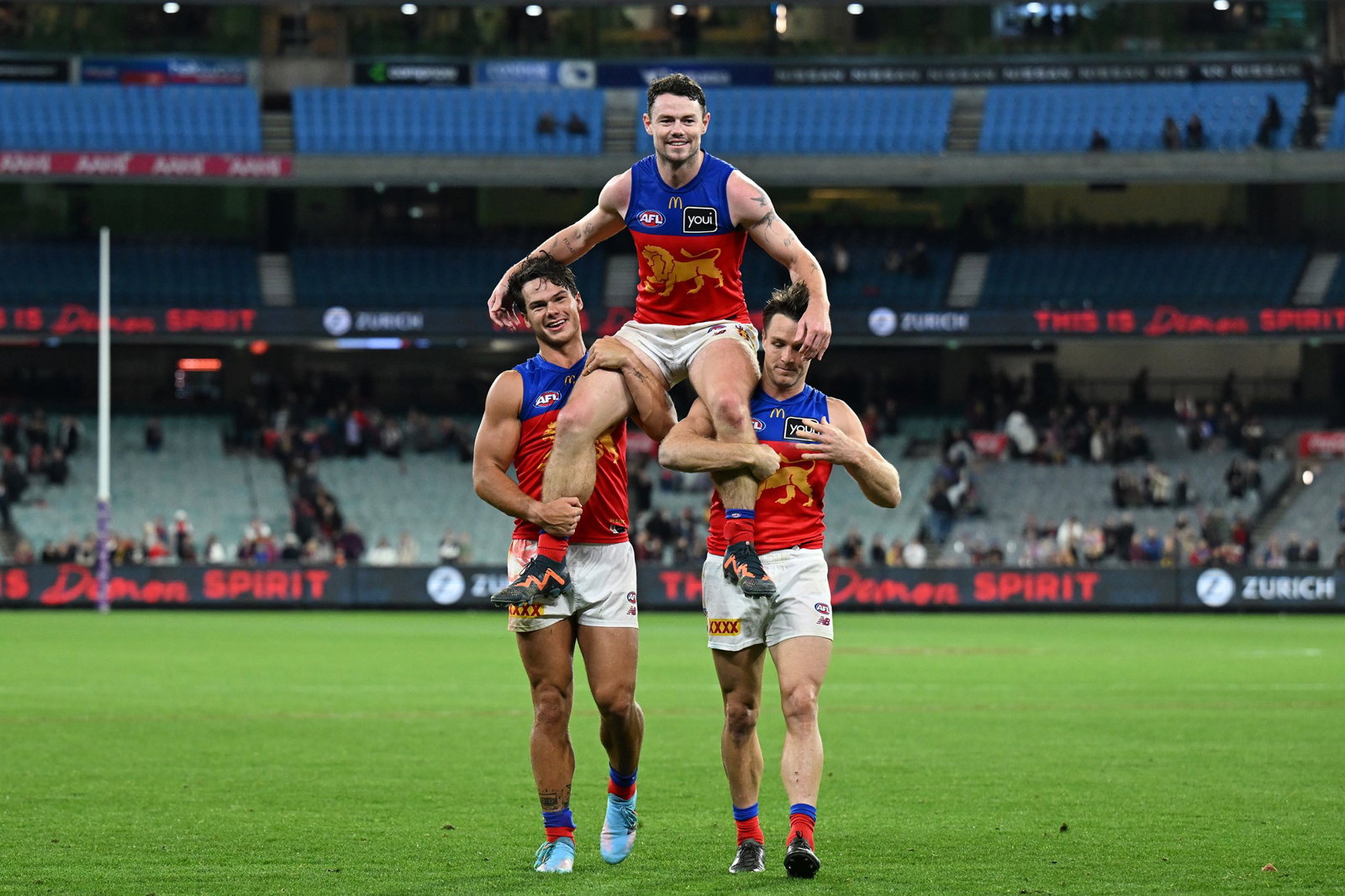 Lachie Neale of the Lions (centre) is chaired of the ground by Cam Rayner of the Lions (left) and Lincoln McCarthy of the Lions after playing his 250th game in the AFL Round 5 match between the Melbourne Demons and the Brisbane Lions at the Melbourne Cricket Ground in Melbourne, Thursday, April 11, 2024.