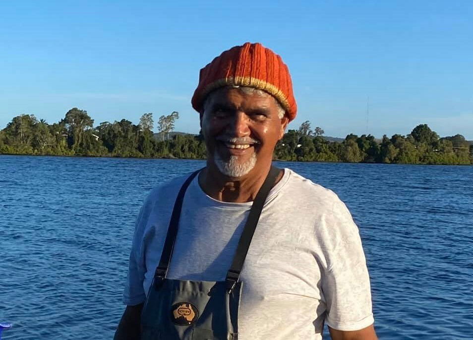 An Indigenous man in a red beanie standing in front of a lake