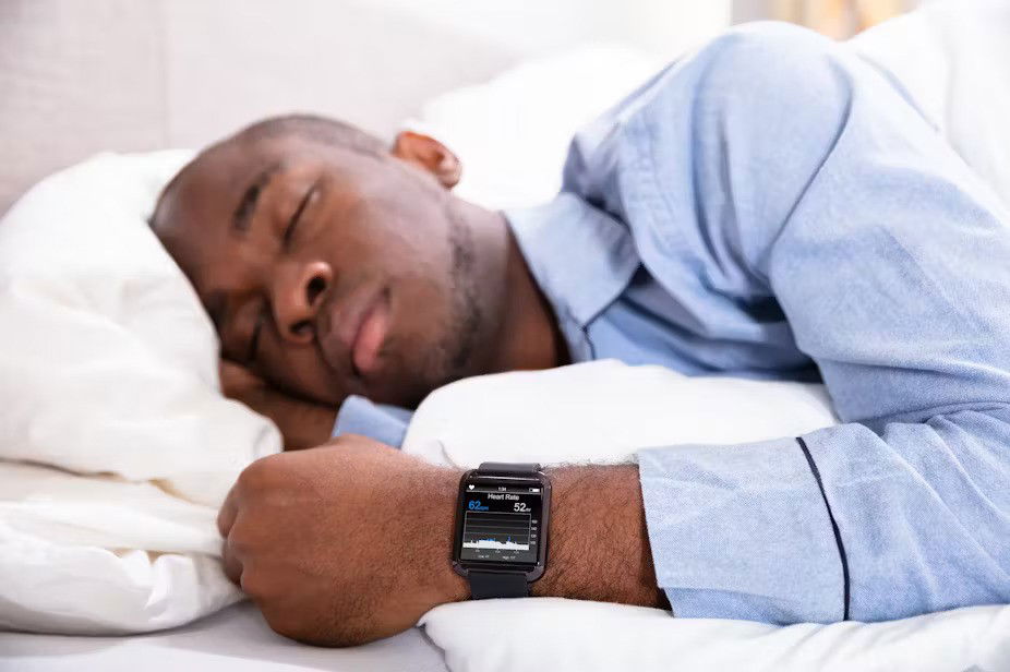 A man in bed with pyjamas on with eyes closed wears a wearable tracker