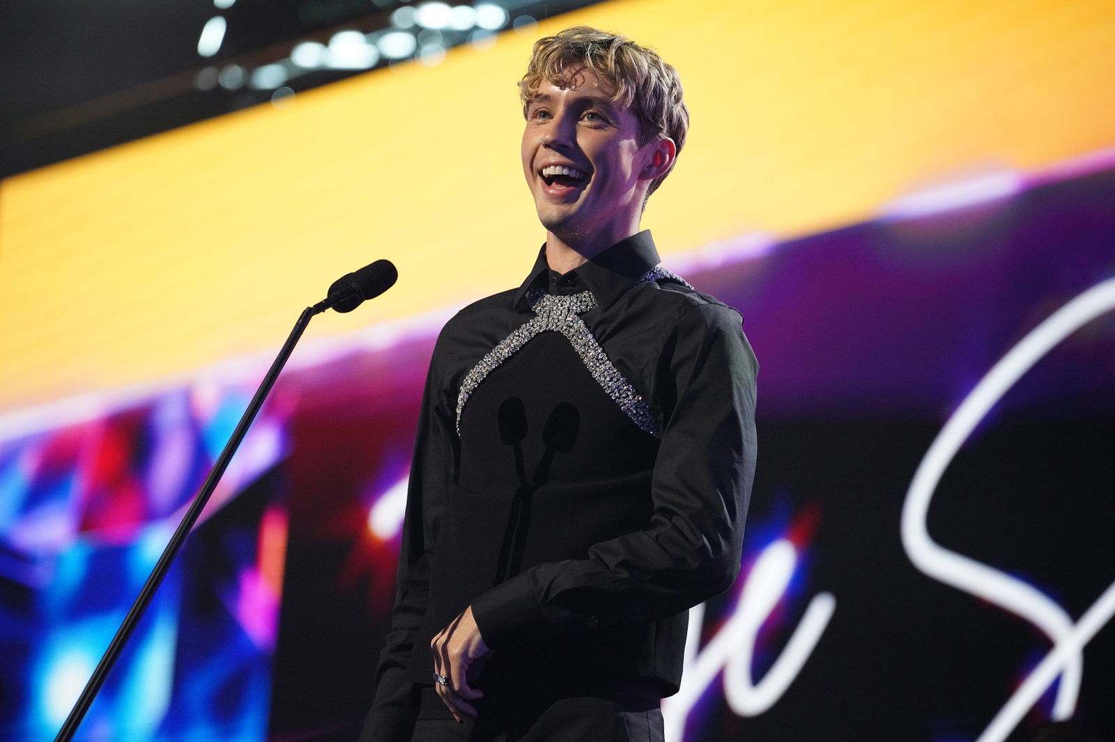 Troye Sivan speaking into a microphone in front of a blurred background