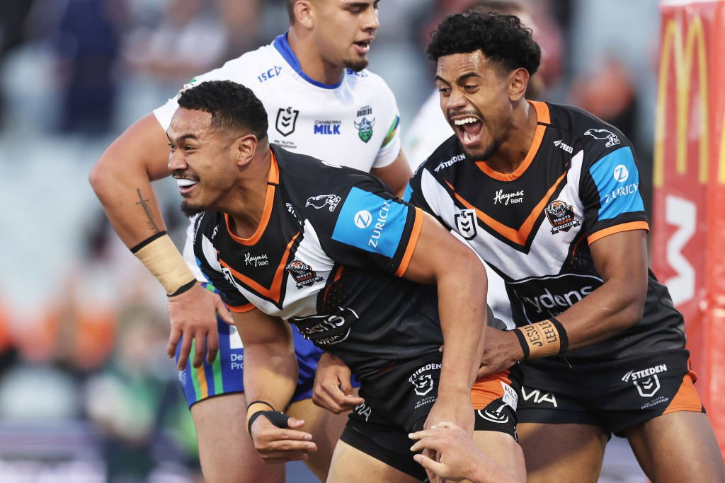 Jahream Bula hugs Wests Tigers Sione Fainu from behind after a try in an NRL game.