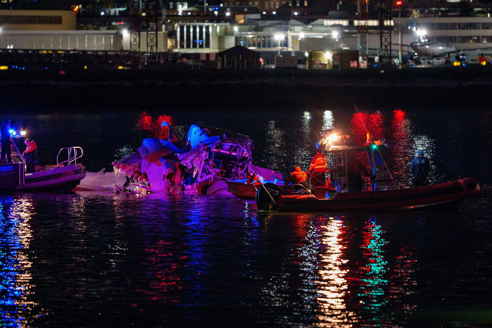 Multiple boats try to haul up a piece of aircraft wreckage in the water at night