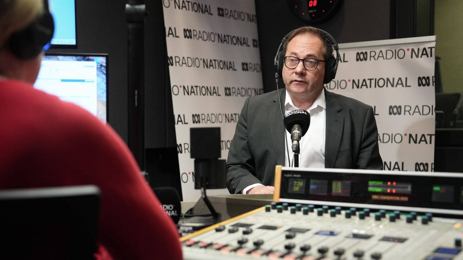 A man sits in front of a microphone at a radio studio. 