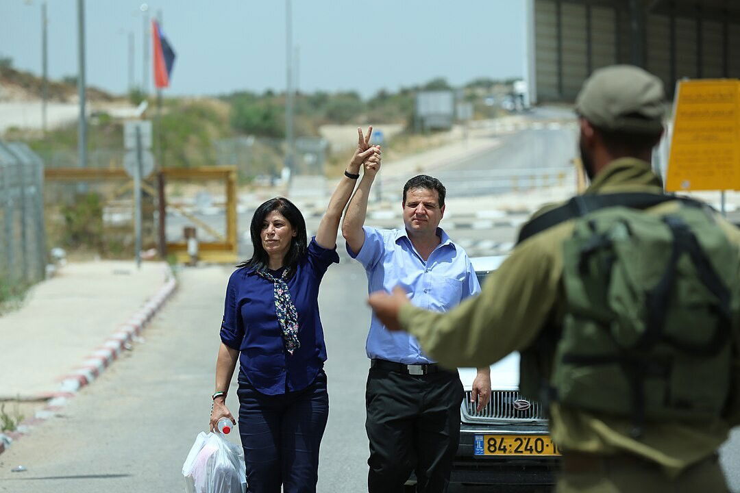 A woman and a man walking away from a prison with their hands in the air.