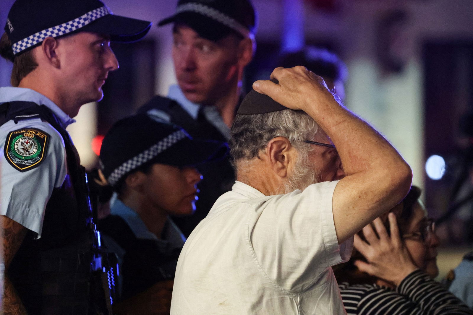 A member of the Jewish community reacts as he walks with police towards the scene of a shooting at Bondi Beach in Sydney on December 14, 2025