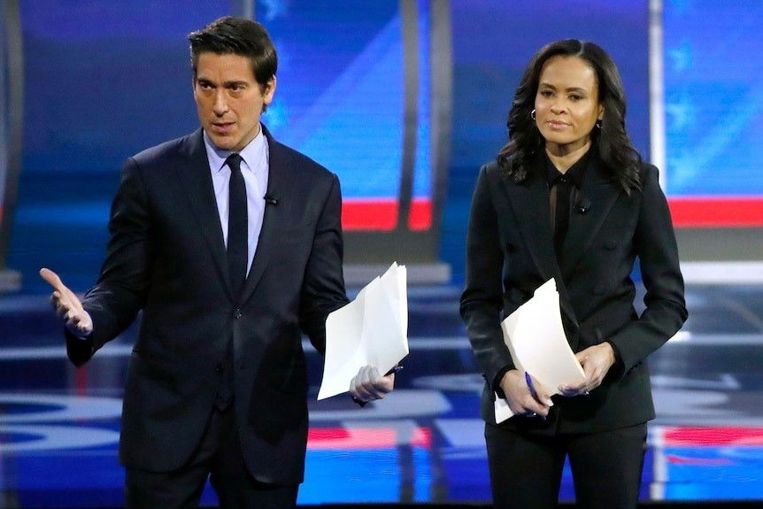 David Muir and Linsey Davis stand in suits in a television studio, holding pages of notes in their hands.