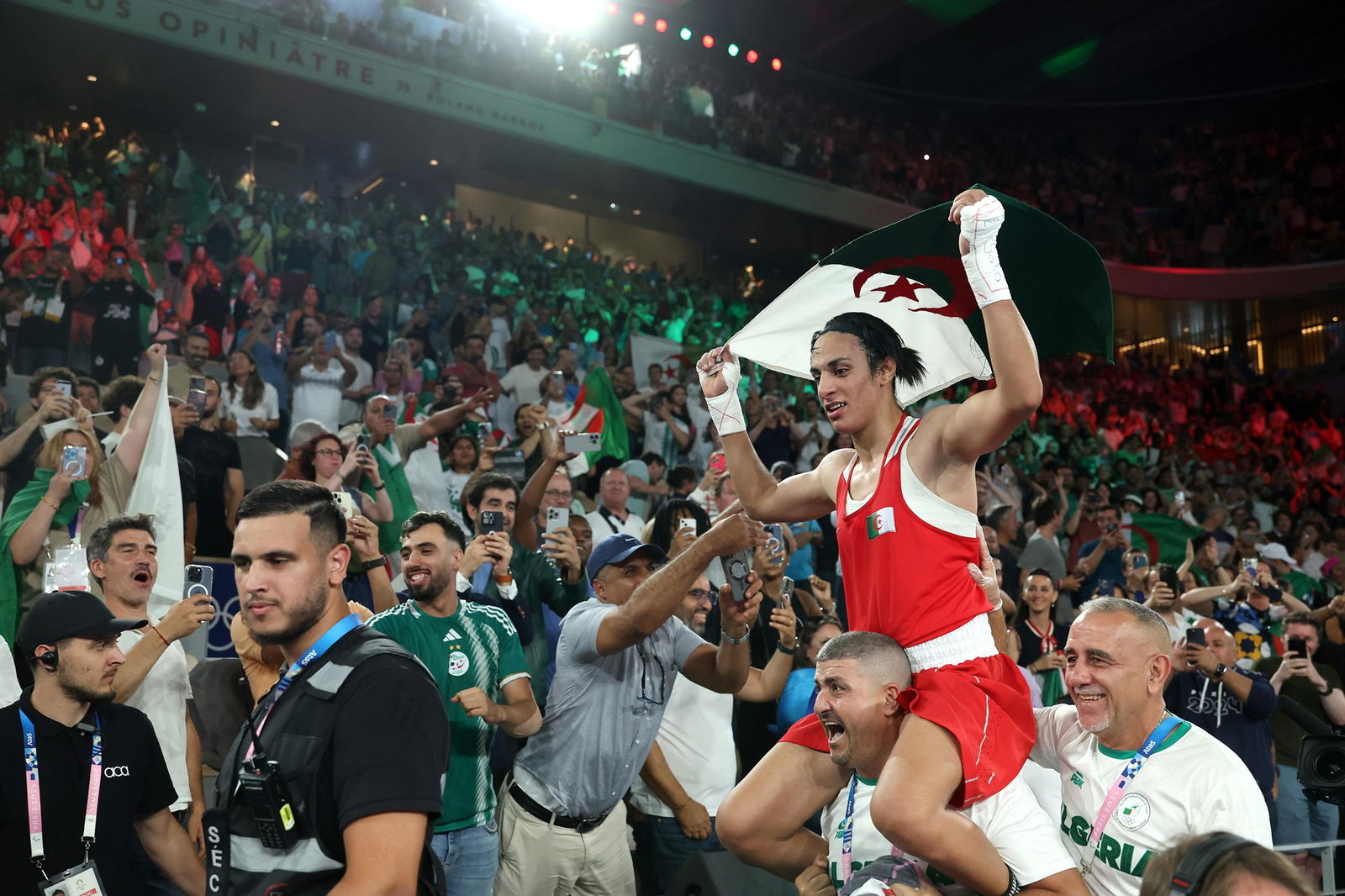 Imane Khelif holds the Algerian flag above her head as she is hoisted on a man's shoulders after winning boxing gold.