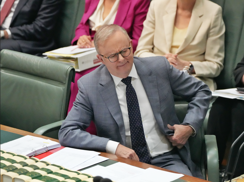 A man in a grey suit sits with eyes closed