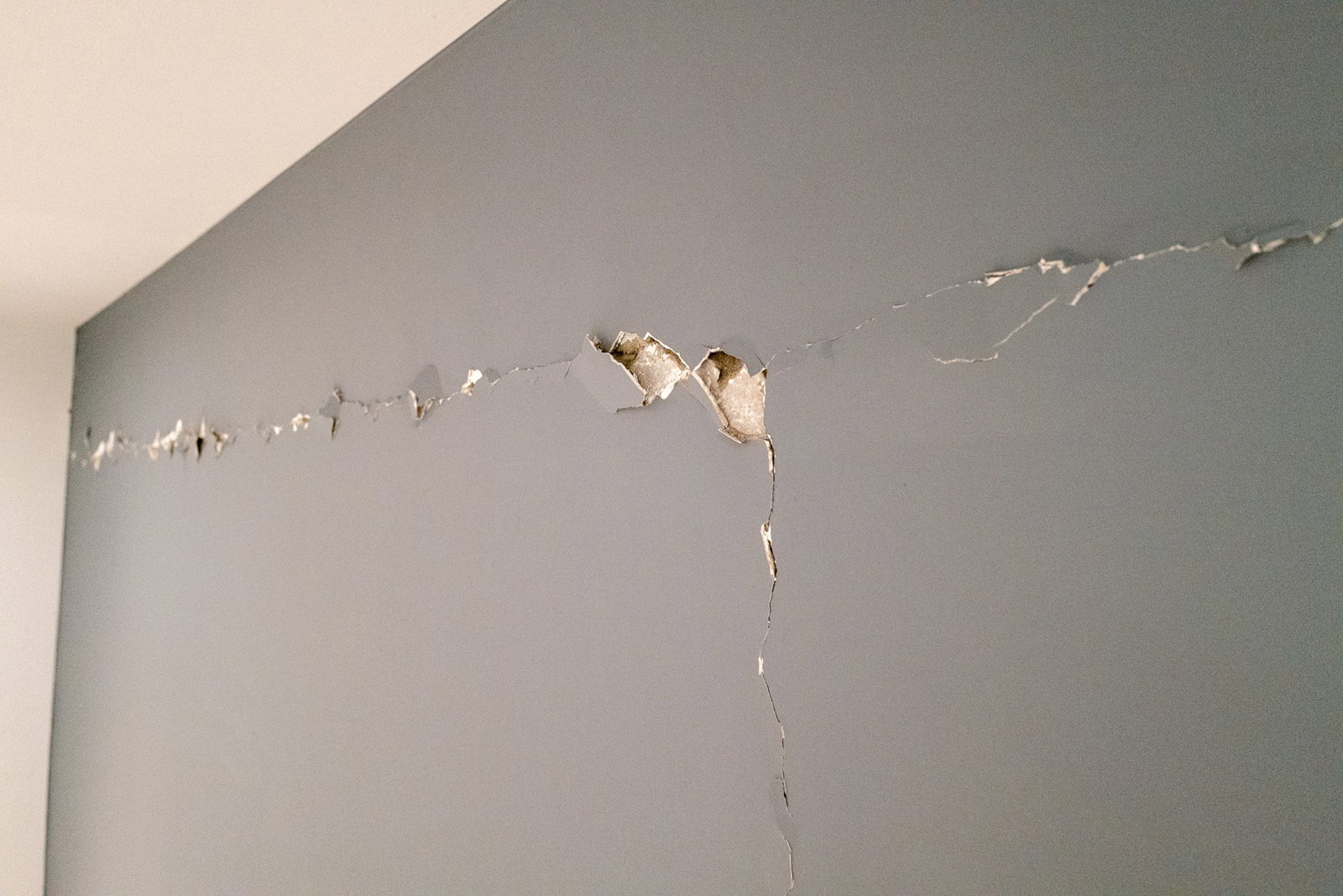 A crack appears in a grey wall with some installation showing.
