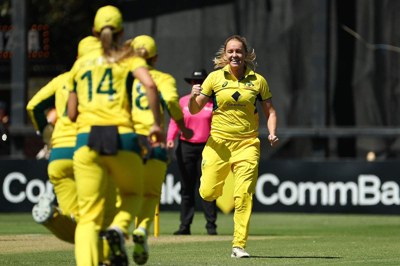 Three women in yellow Australia cricket jerseys celebrate a wicket.