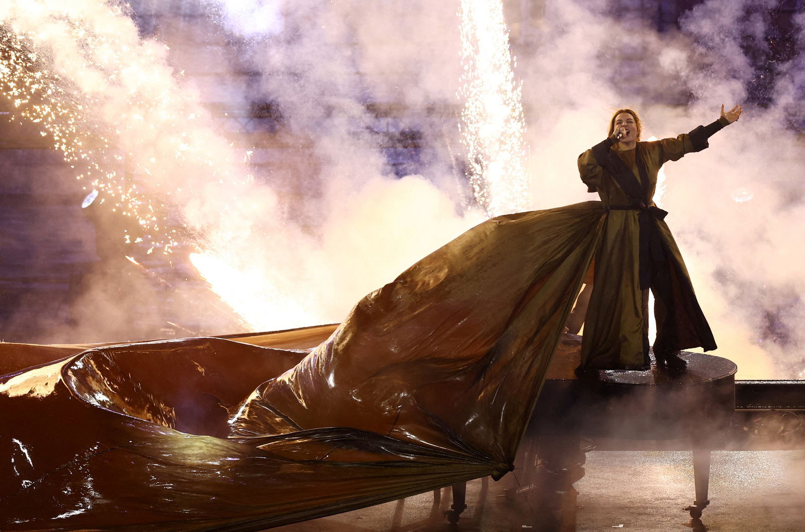 Female artist in a long dress singing with fireworks behind her