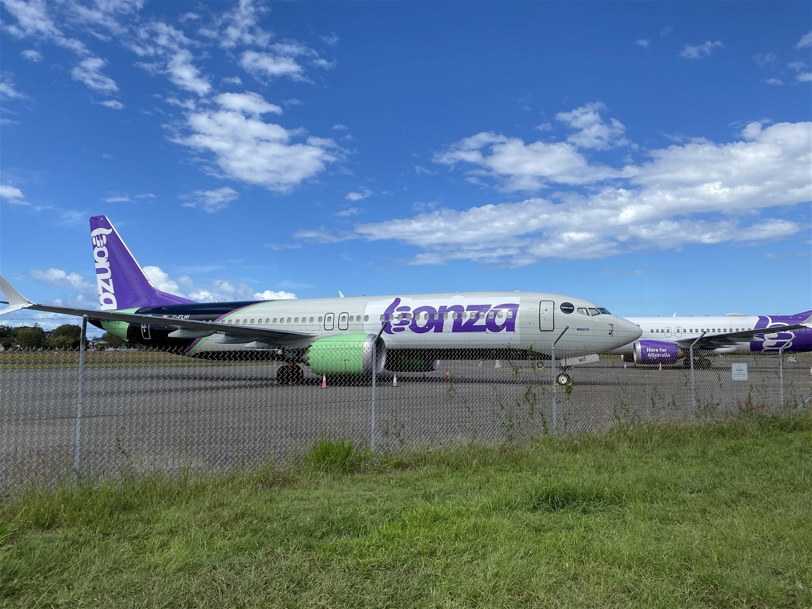 Image of gras, a gate and behind it, a Bonza airplane.