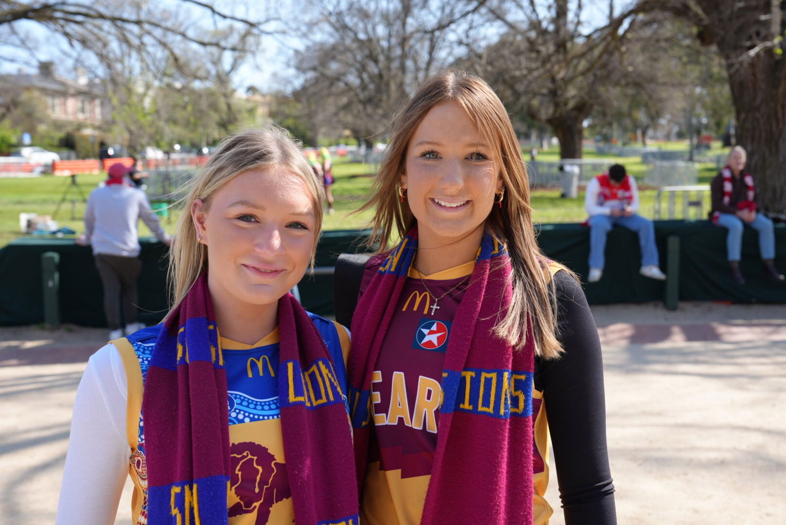 Torah Pratt and Tilly Saunders, decked out in Lions gear, smile in the sunshine outside the MCG.